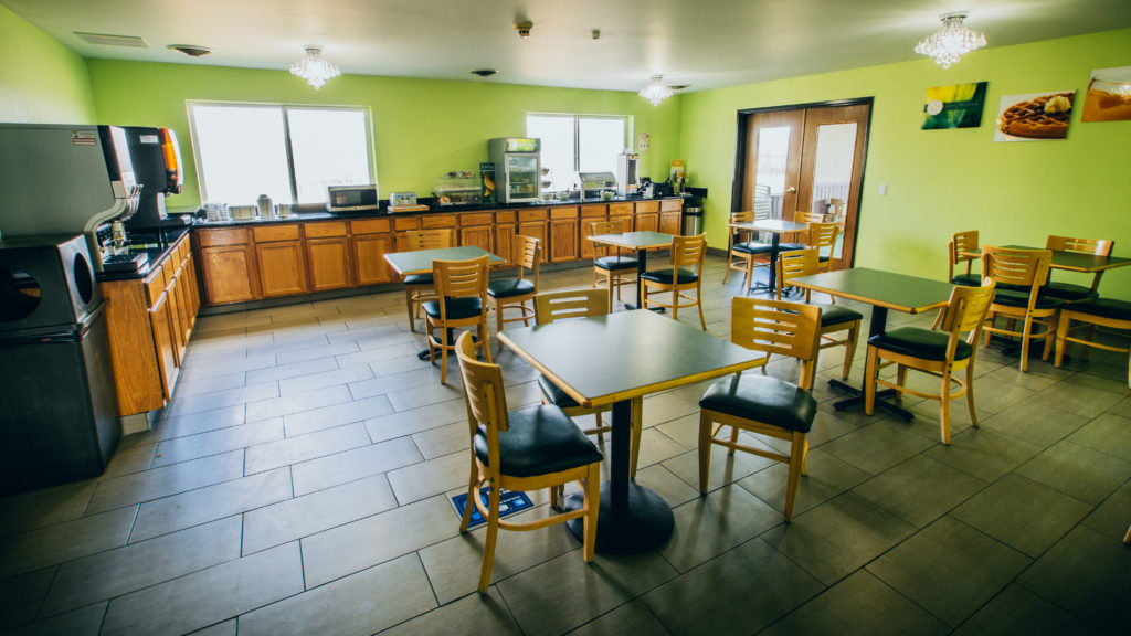 The breakfast area features green walls, several tables for seating, a breakfast bar and machines for beverages.
