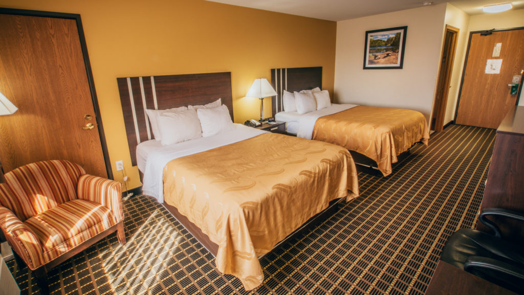 A troom with two beds featuring warm tones on the walls and bed sheets. Two beds lay side by side with an armchair on the left of them.